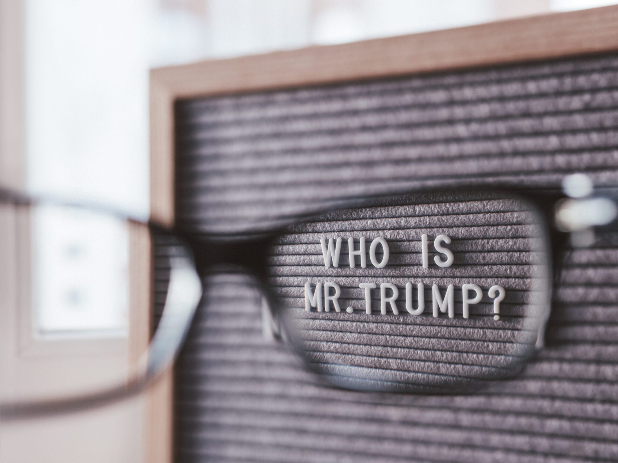 Letterboard with question WHO IS MR.TRUMP? through eyeglasses. C